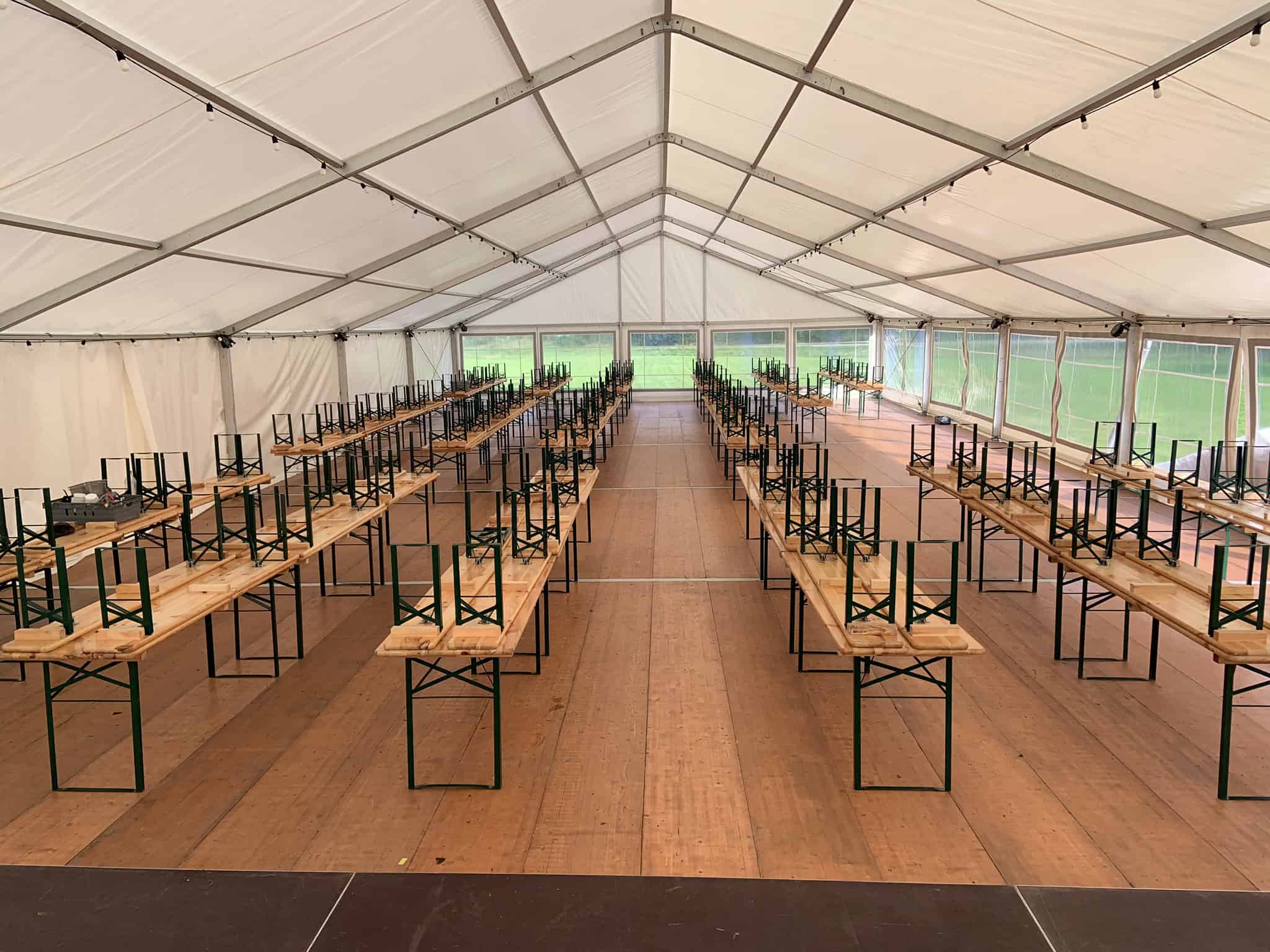 Bänkset från Kikiriki som skapar långbord inuti ett Sektionstält med golv för ett stort event