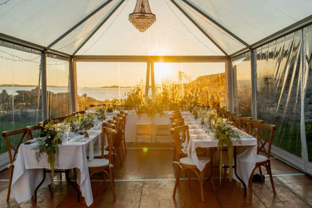 Elegant bröllopsfest i ett tält med utsikt över havet och solnedgång.